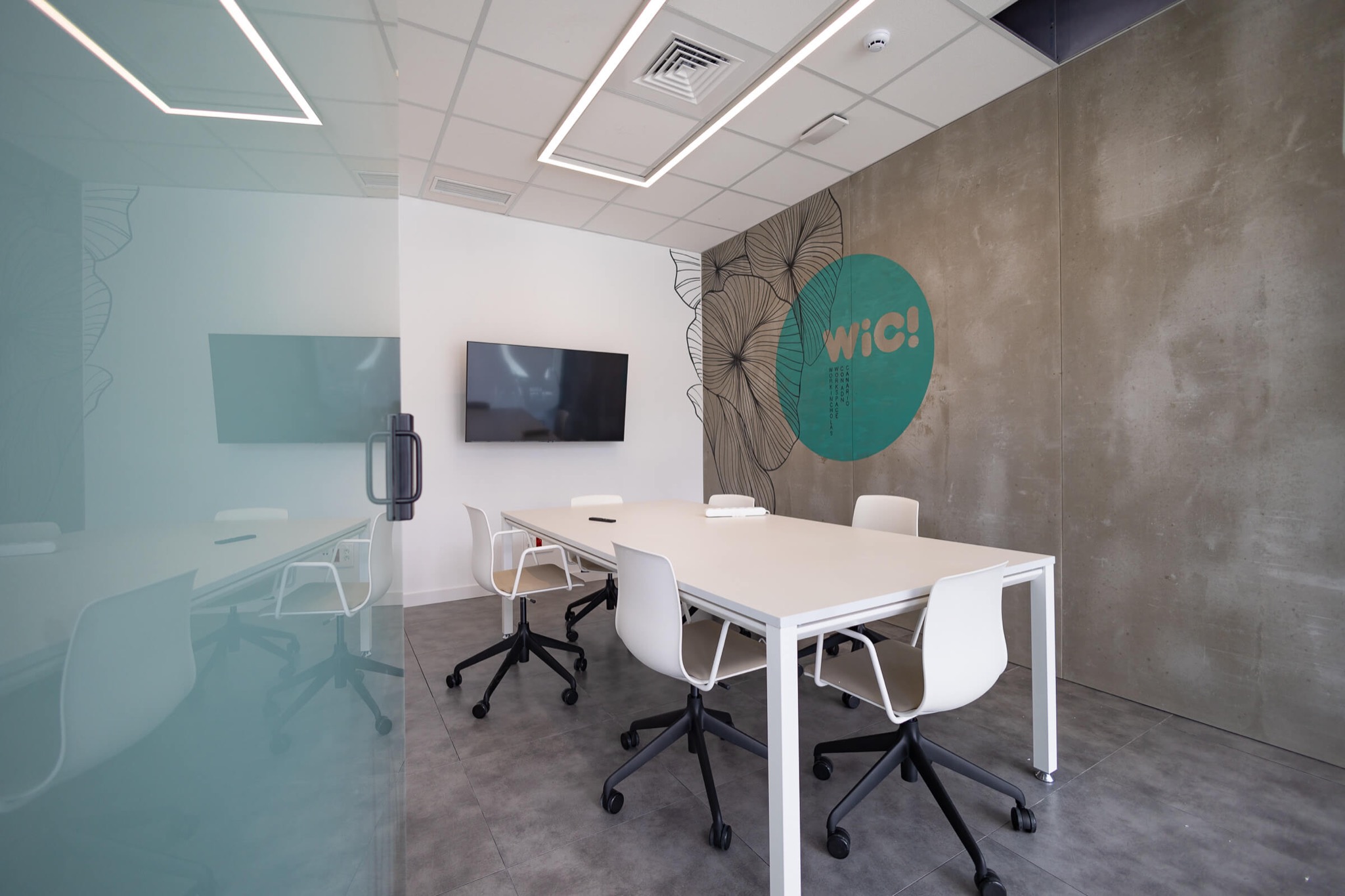 Sala de reuniones flip de WiC! La Minilla, con mesa para seis, pantalla y mural de marca.